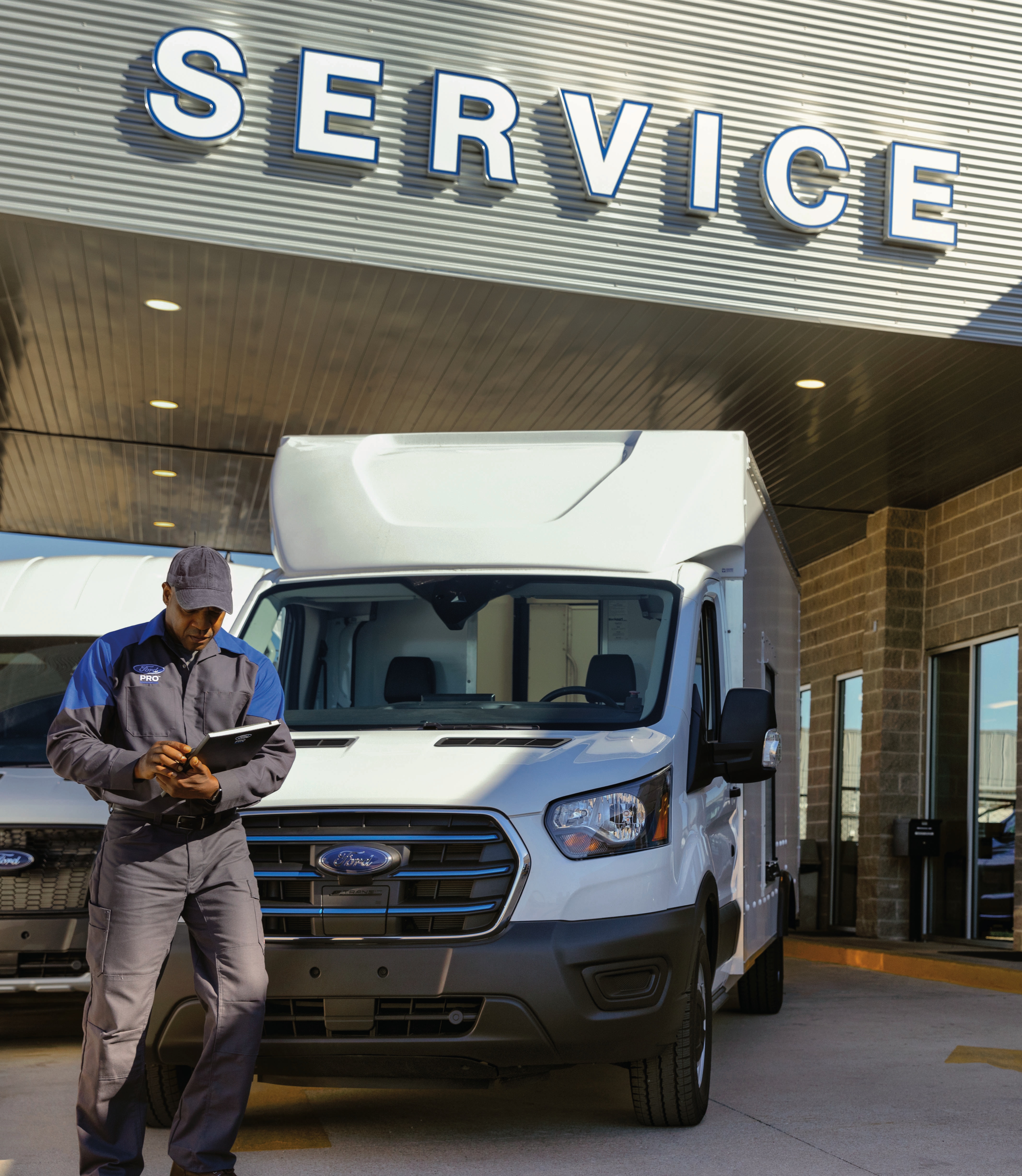 A man looks at a tablet in front of a work truck parked under an awning that says "service"